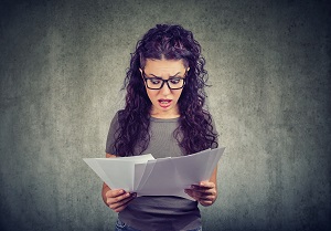 woman glasses exploring papers from bank with list of bills and fees looking stressed on gray background | are hoa fees negotiable