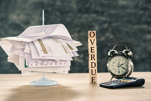 stack of unpaid bills, calculator and clock on table | late hoa dues
