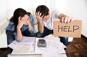 young couple worried and in stress at home couch and the man is holding out a cardboard with the word help written on it | financial problem
