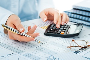 man using a calculator while reviewing financial reports and holding a pen | hoa finances