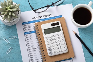 Monthly budget document with white calculator and coffee cup on blue wooden table | transparency of budget